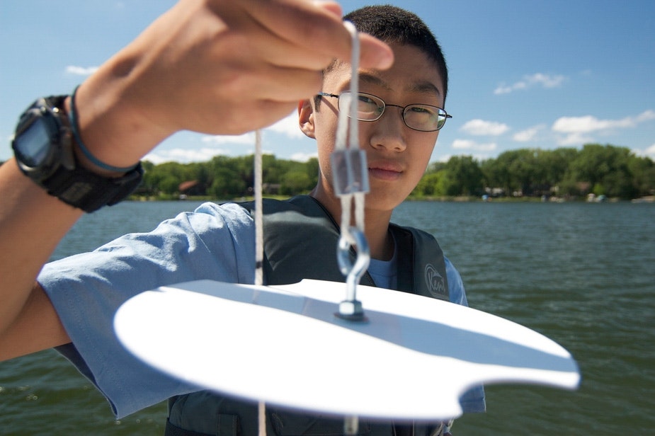 A person holding a Secchi disk on a boat near a body of water, used for measuring water clarity.