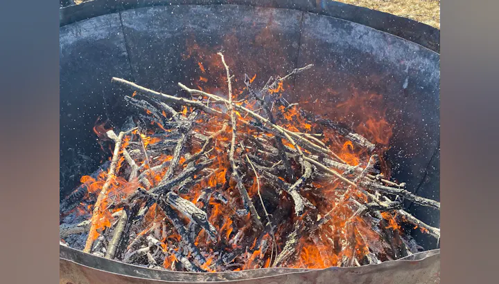 A bonfire with burning sticks and visible flames inside a metal container.