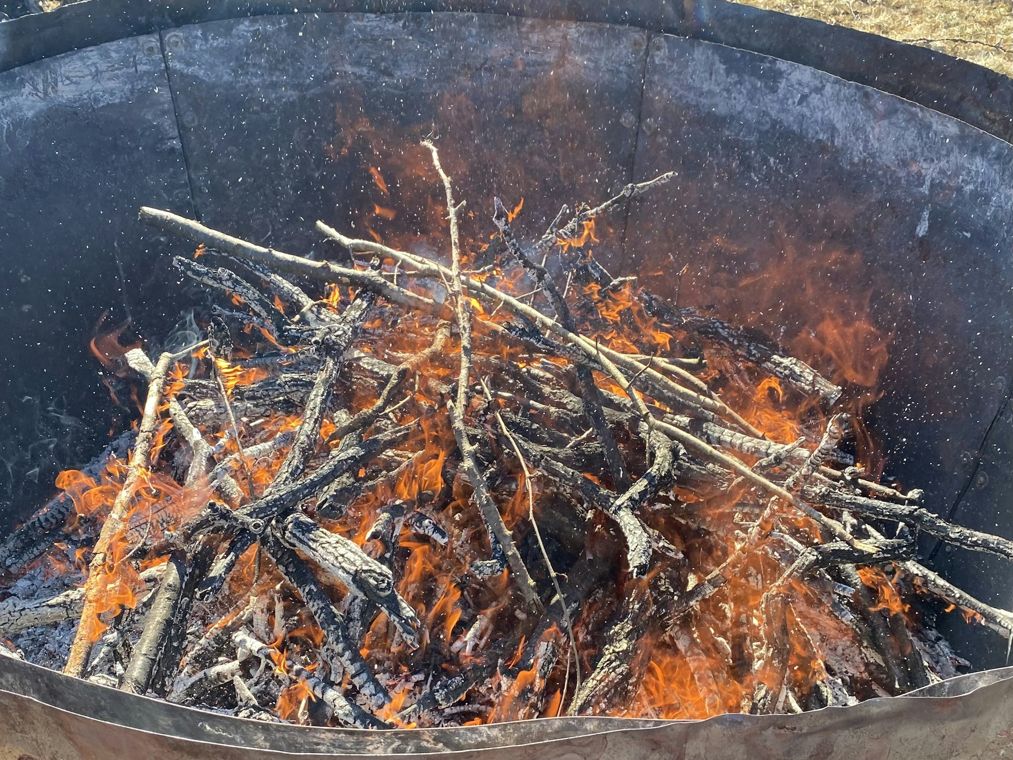 A bonfire with burning sticks and visible flames inside a metal container.