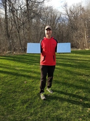 A person in a red hoodie holds two white panels outdoors on a grassy area with bare trees in the background.