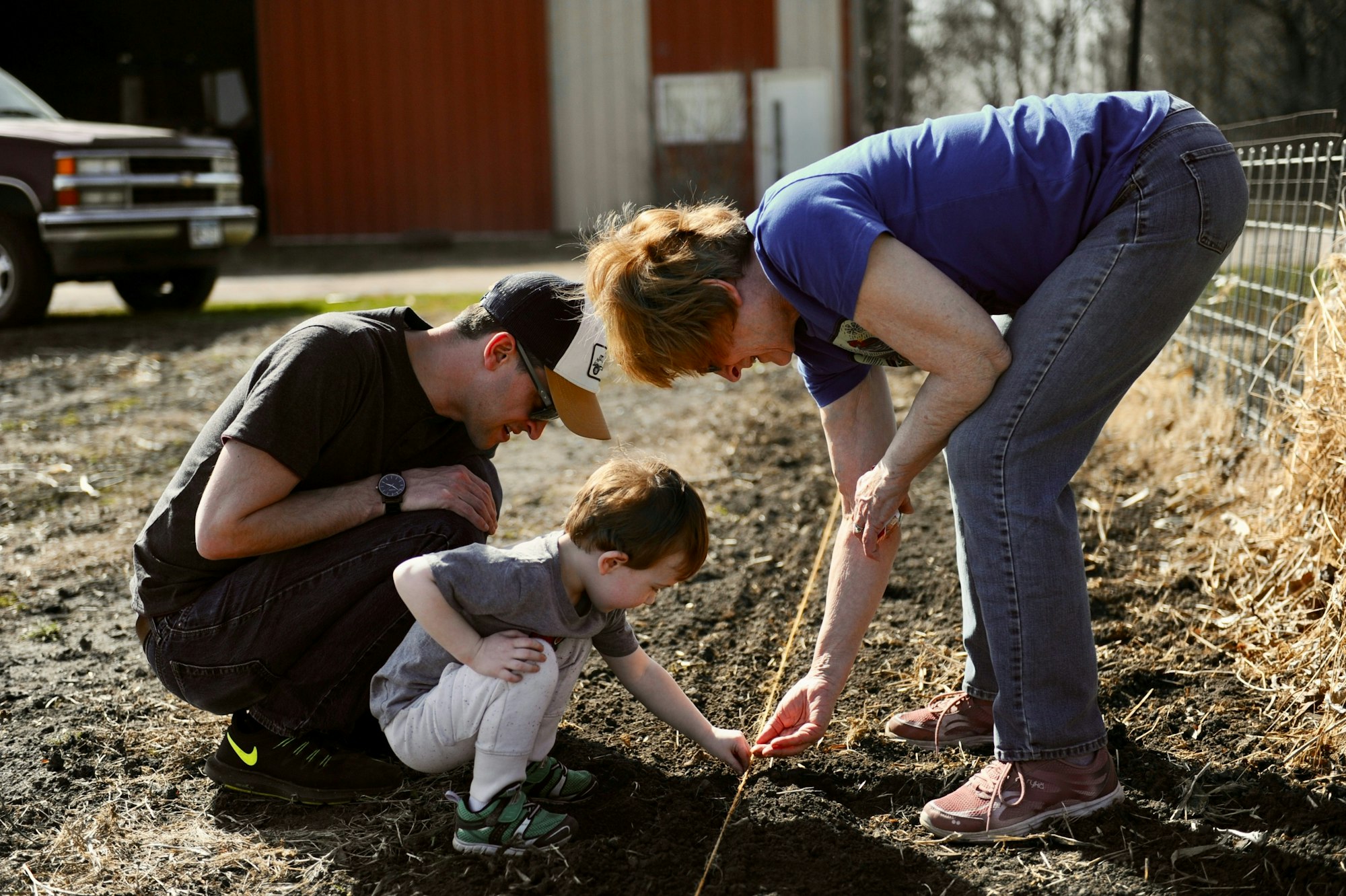 Three people gardening, with a child helping plant seeds in the soil.