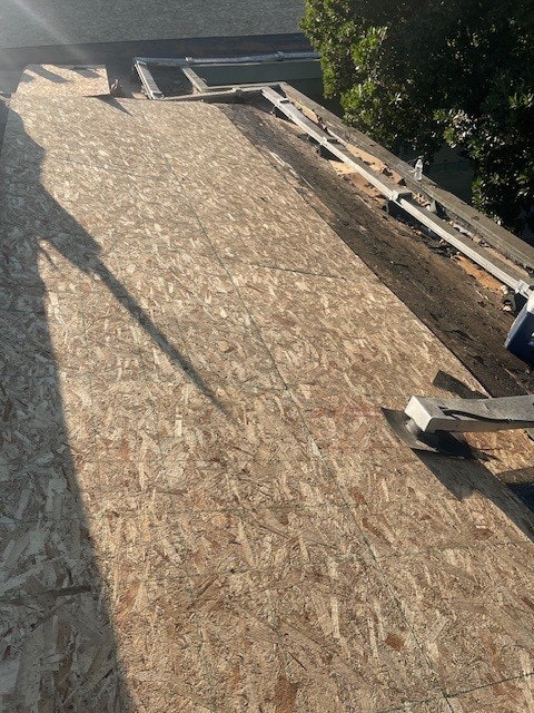 A section of a roof under construction with wooden boards and exposed beams, in sunlight.