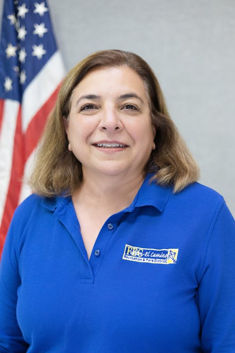 A person in a blue shirt with a logo stands in front of an American flag.