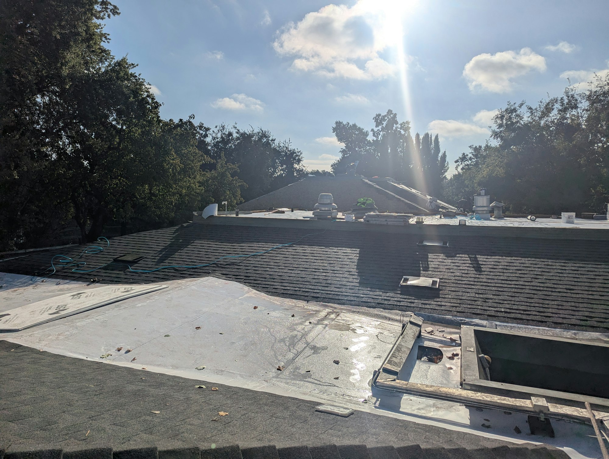 A rooftop with construction materials, a ladder, and a sunny sky with scattered clouds in the background.