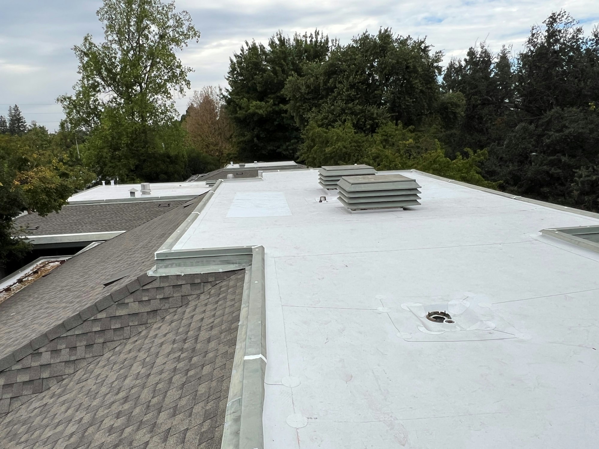 Flat rooftop with vents, surrounded by trees, cloudy sky.