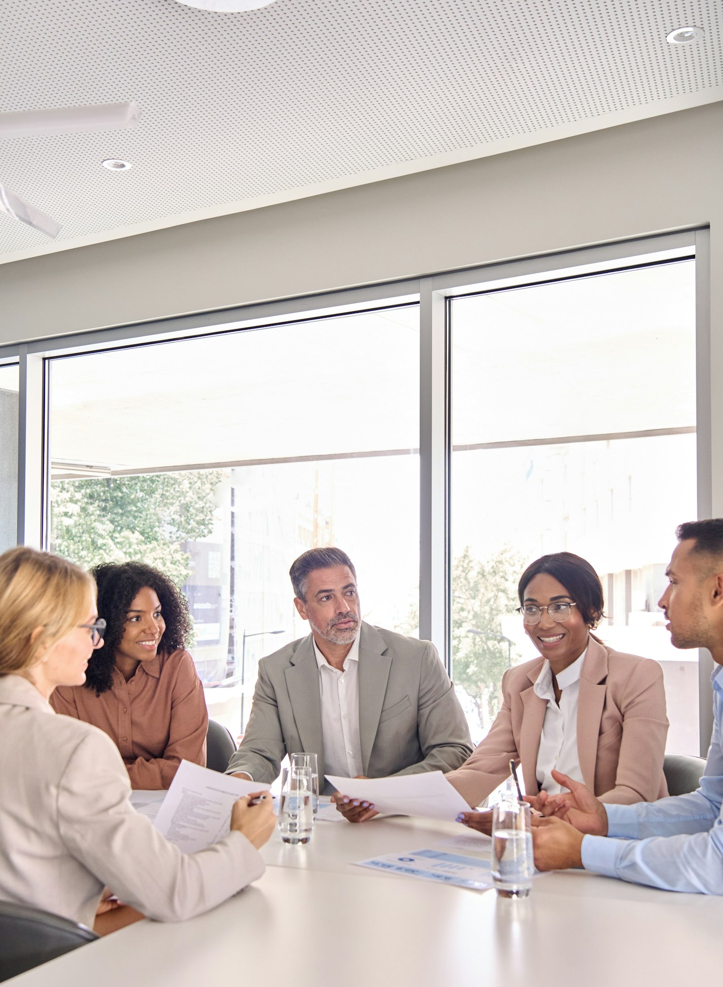 Five people in a meeting room, sitting around a table with documents and glasses of water.