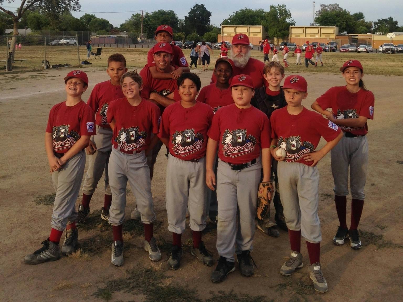 A youth baseball team poses for a photo, wearing red jerseys with a bear logo and grey pants.