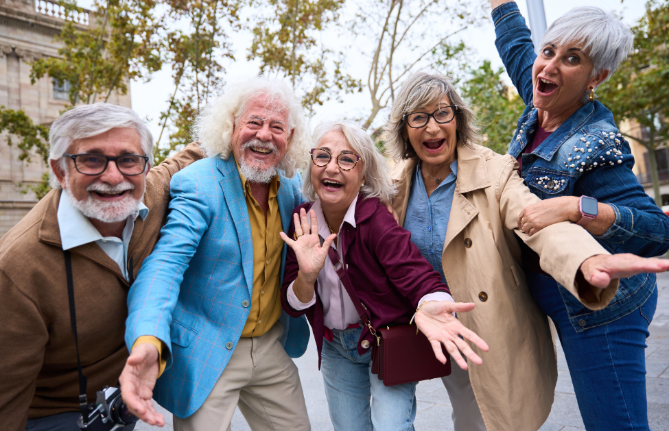 A group of five cheerful older adults posing together outdoors, smiling and expressing joy.