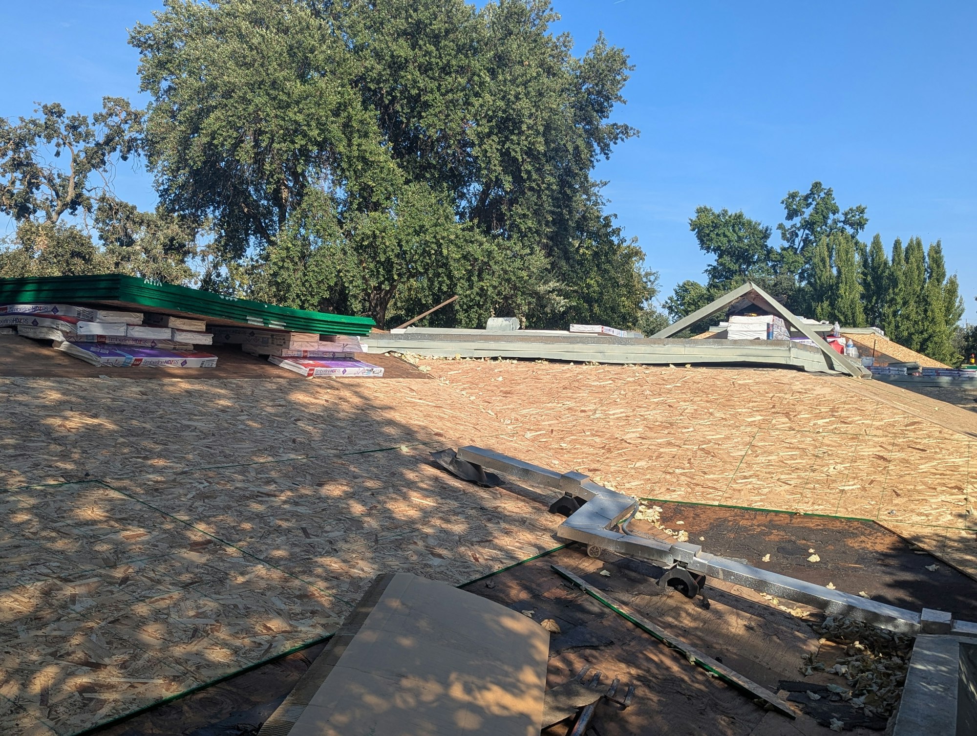 Construction materials on a rooftop under blue sky, with trees in the background.