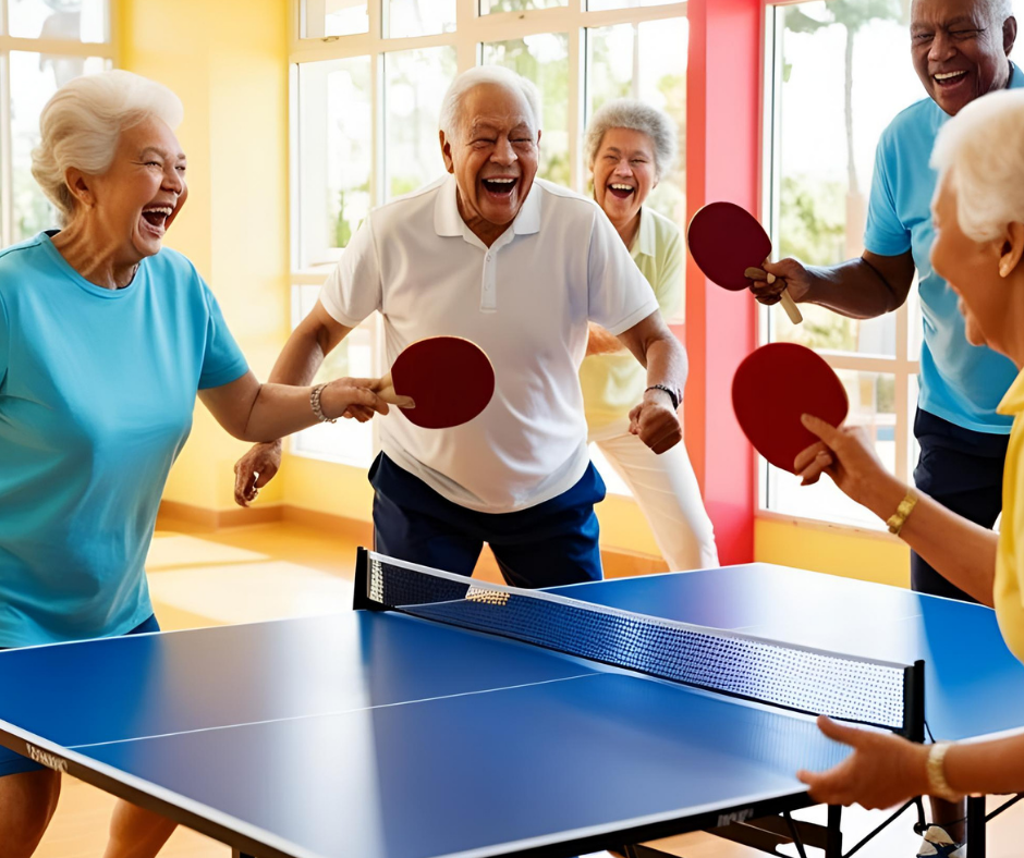 Group of seniors joyfully playing table tennis indoors with paddles, net, and bright surroundings.