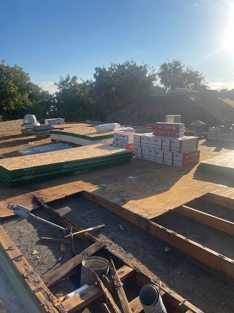 Roofing materials and equipment on a roof under construction with trees in the background.
