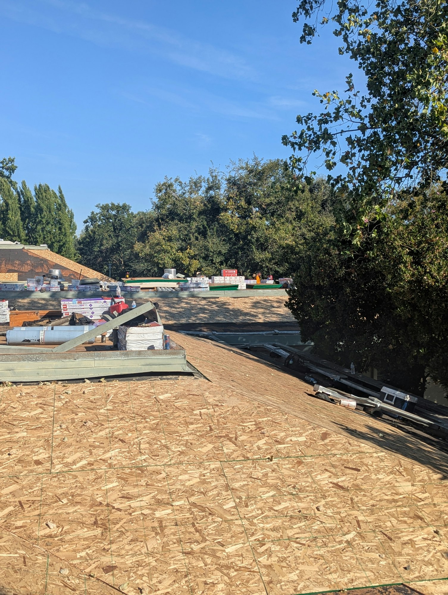 A rooftop under construction with stacks of building materials and trees in the background.