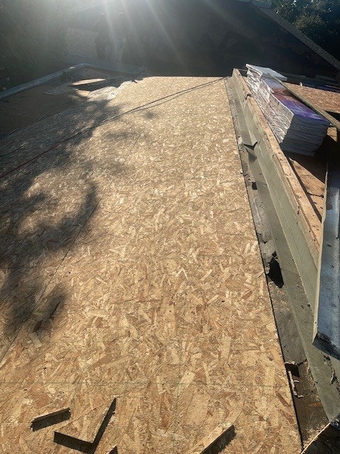 Plywood sheets on a roof under construction with sunlight and a stack of materials on the side.