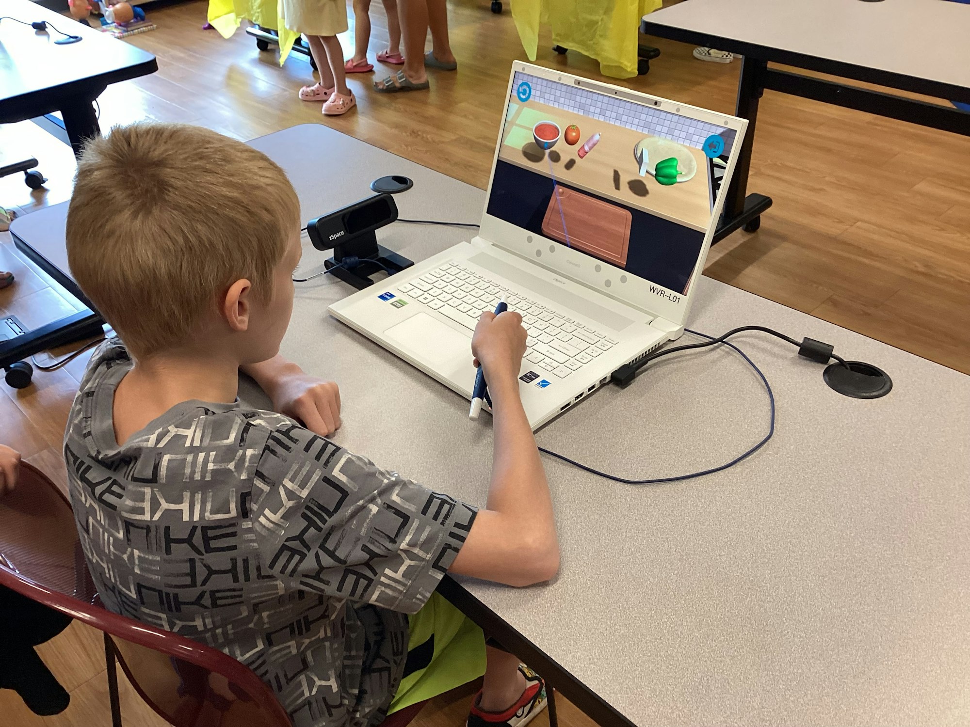 A child uses a laptop at a table, interacting with a digital activity on the screen.