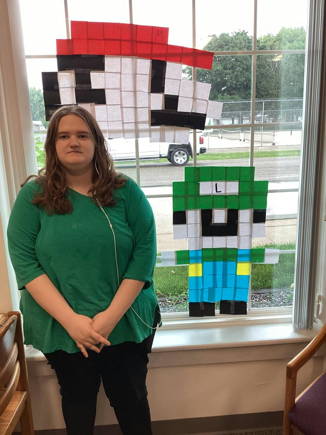 A person stands by a window with pixel art of video game characters made from colored paper squares.