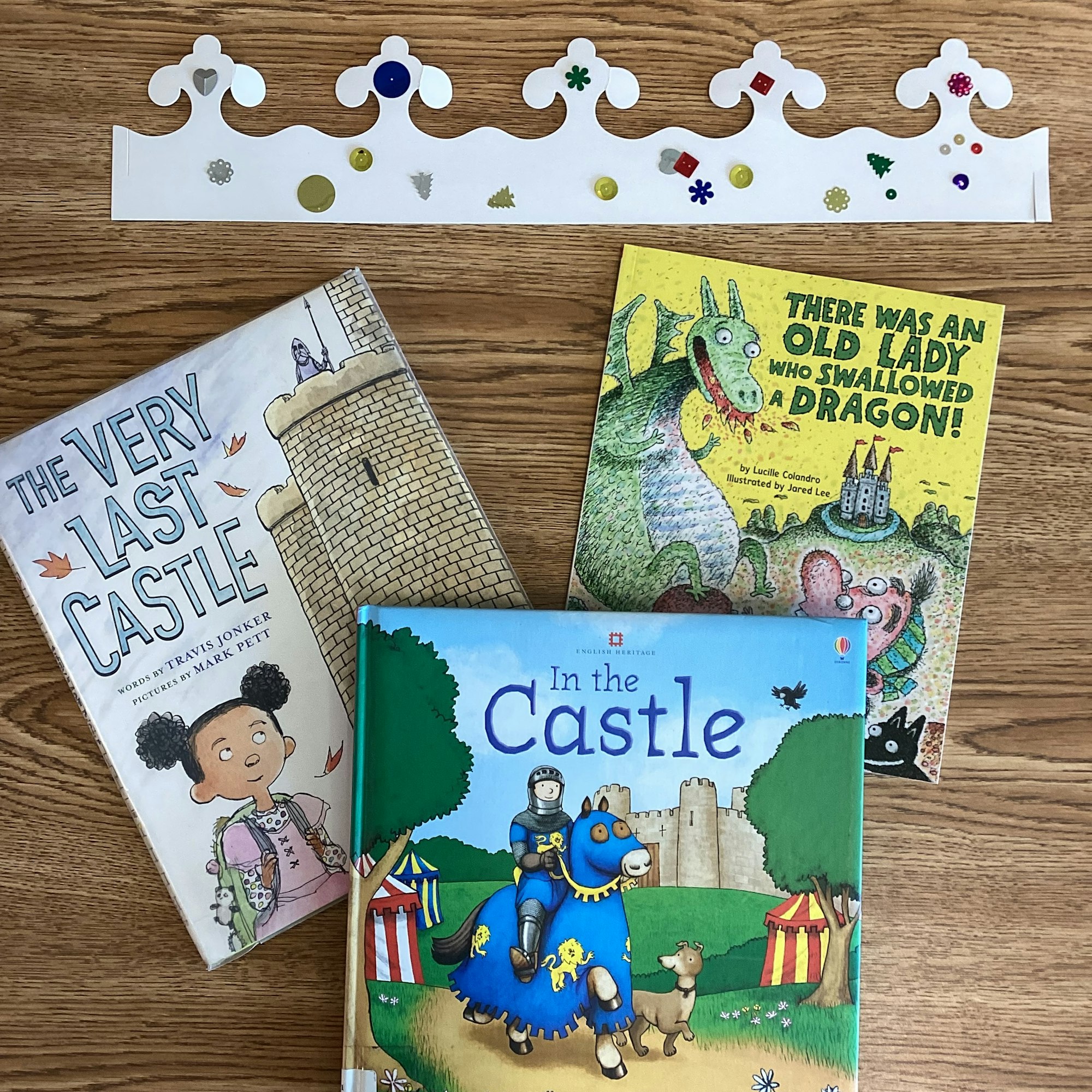 Three children's books and a decorated paper crown on a wooden surface.