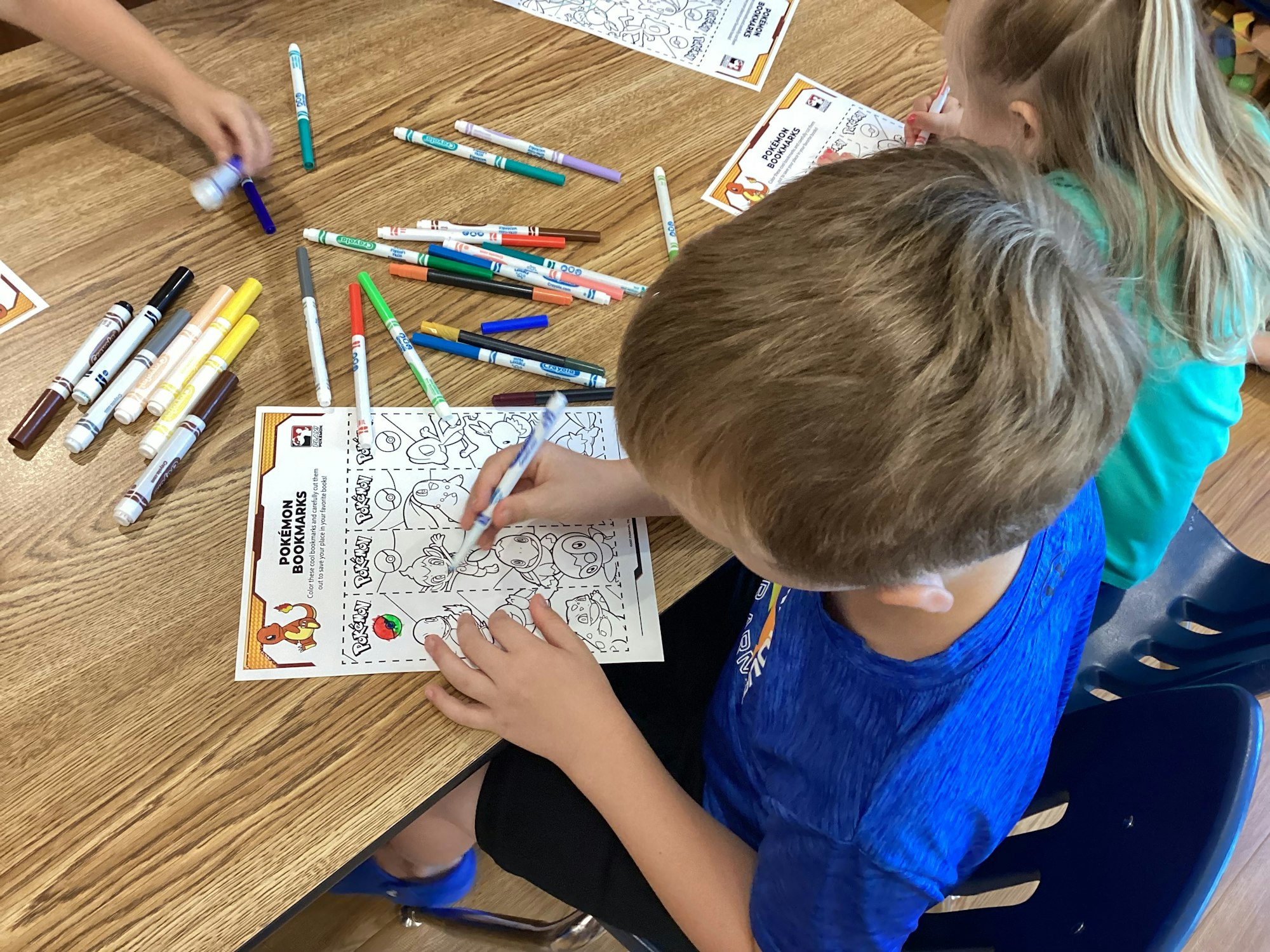 Children coloring Pokémon bookmarks at a table with markers.