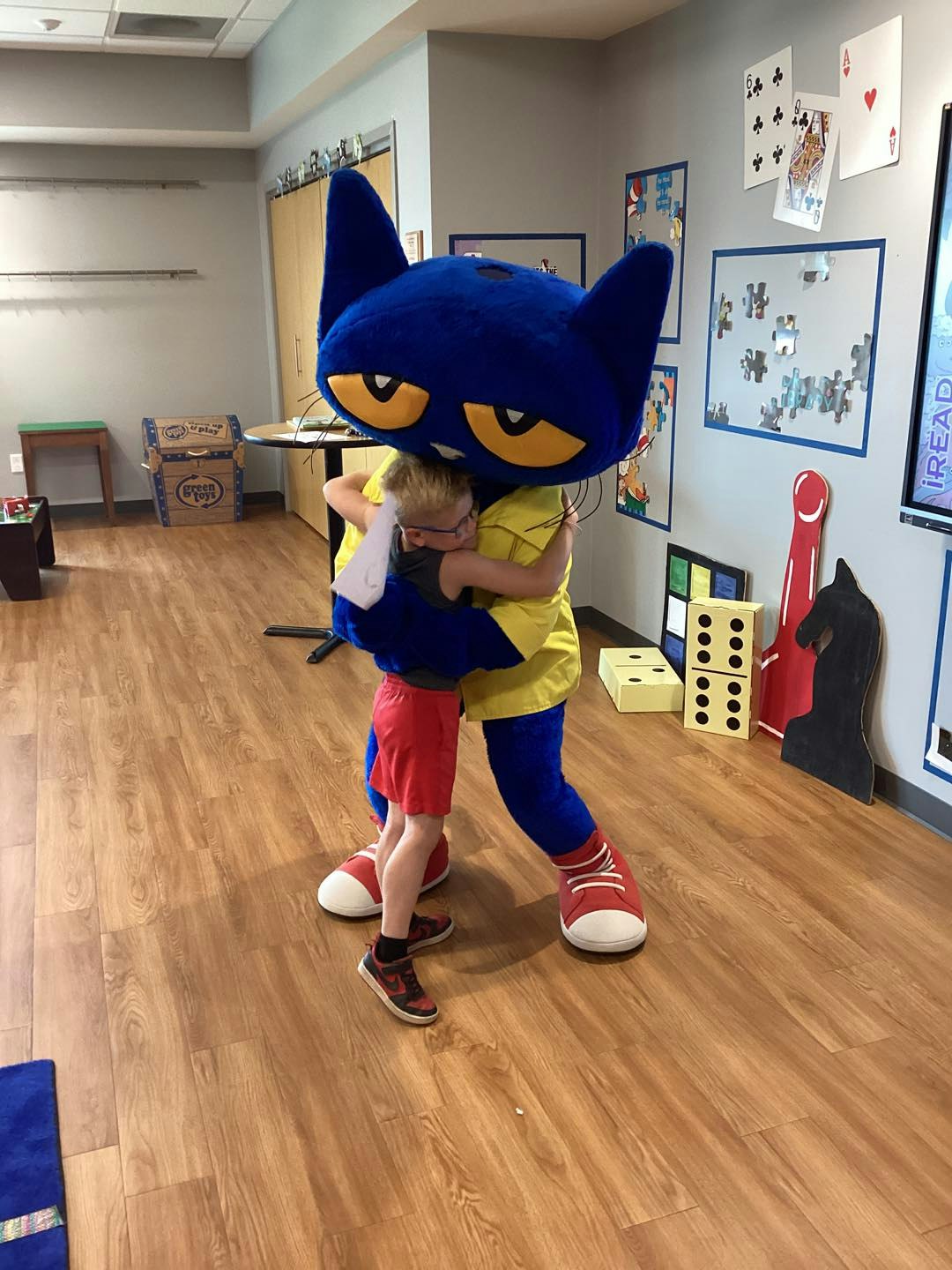 A child is hugging a person in a large blue cat costume in a playroom.