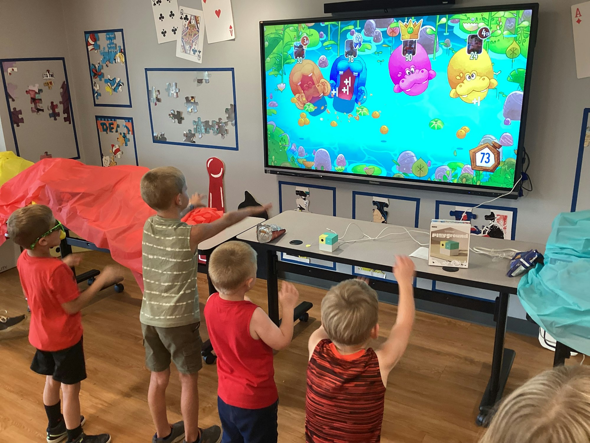 Kids playing an interactive game on a large screen in a colorful room with puzzle-themed decor.
