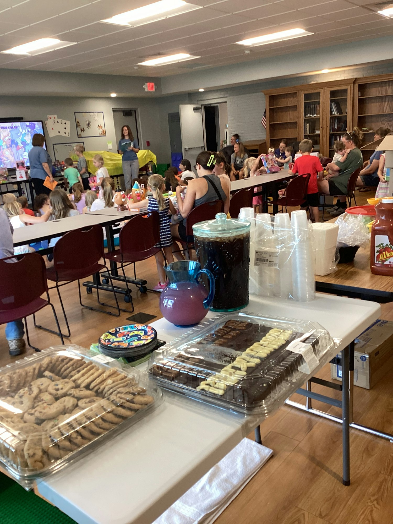 Room with tables, people seated, cookies, and drinks. Looks like an event or gathering.