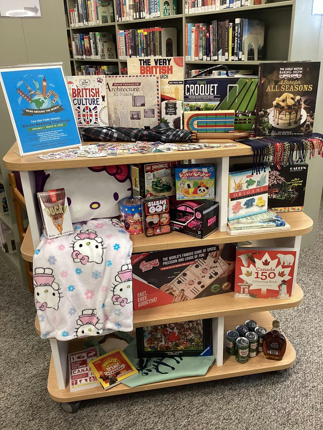A library display with books, puzzles, games, a blanket, and snacks, promoting a "Read Around the World" challenge.