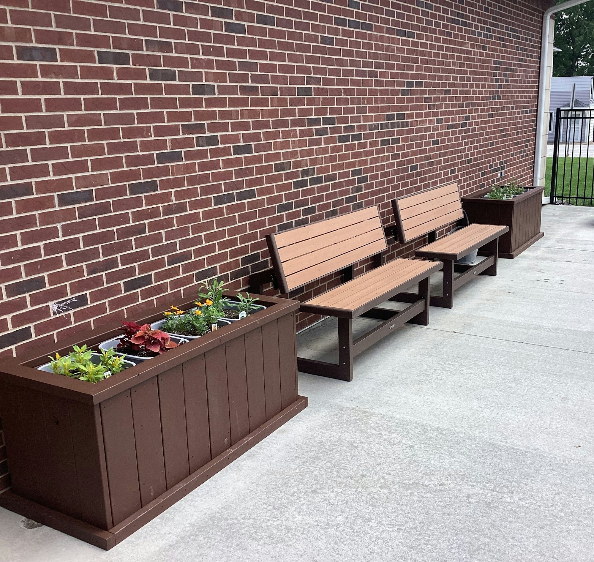 Benches with planters against a brick wall on a concrete surface.