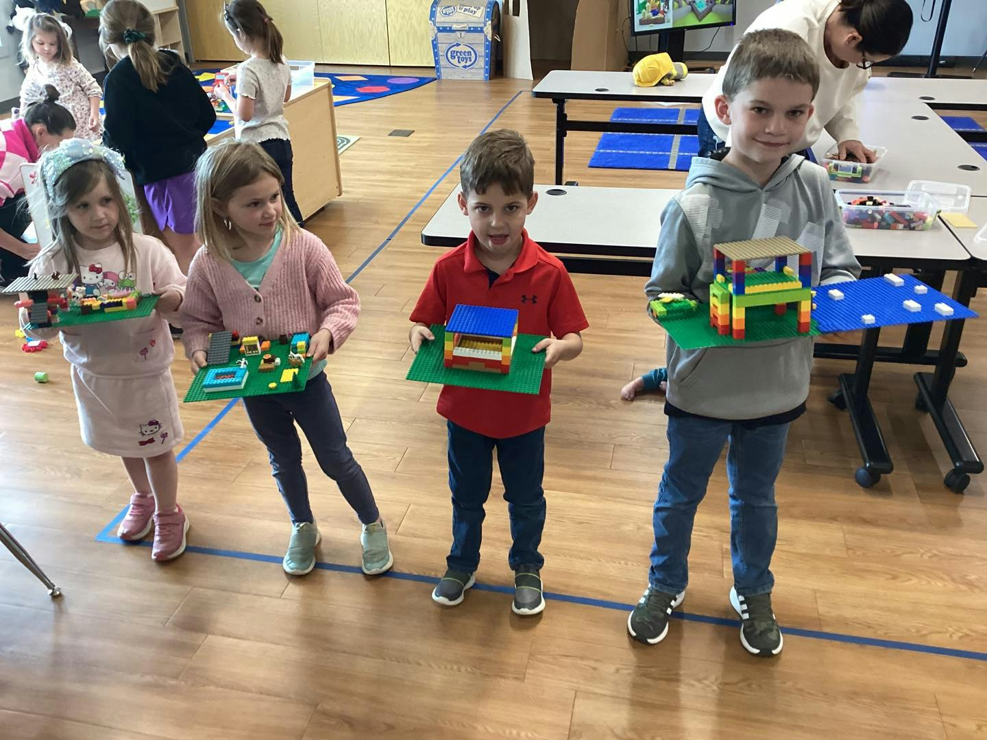 Four kids holding Lego creations in a classroom setting.