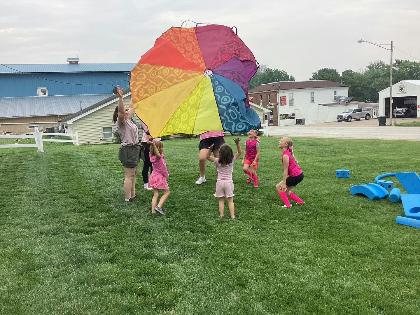 Children playing with a colorful parachute on a grassy field.