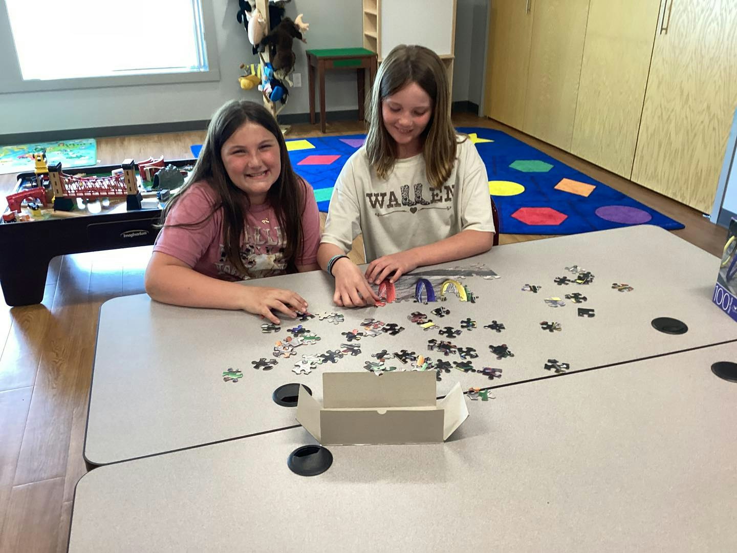 Two kids are sitting at a table working on a jigsaw puzzle in a playroom.