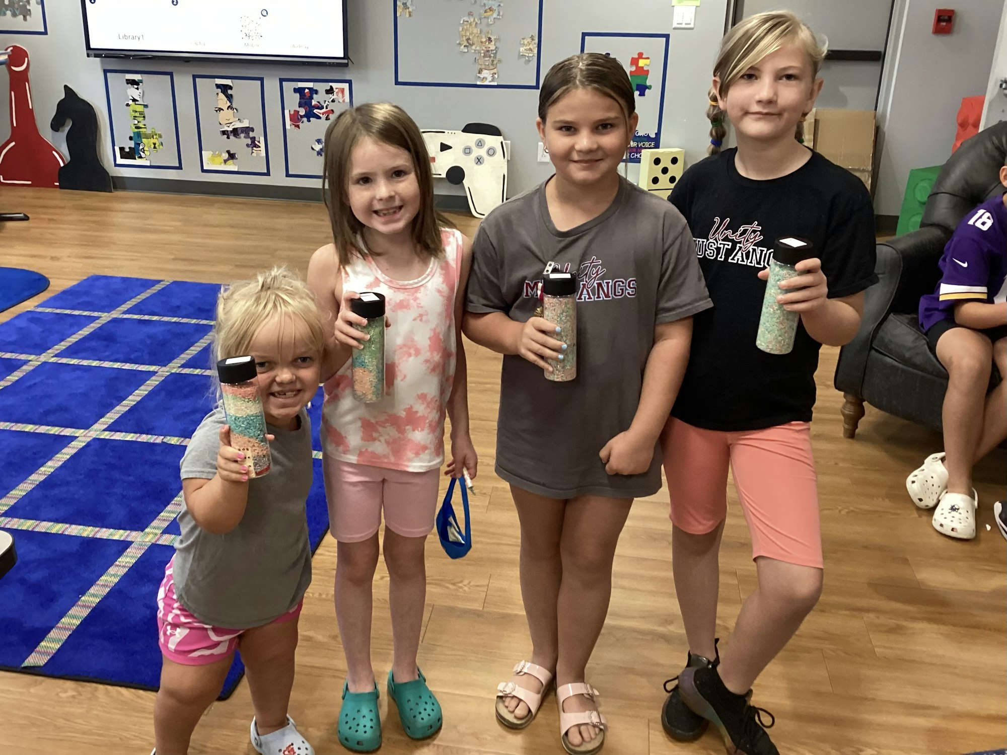 Four kids holding bottles with colored contents, smiling indoors.