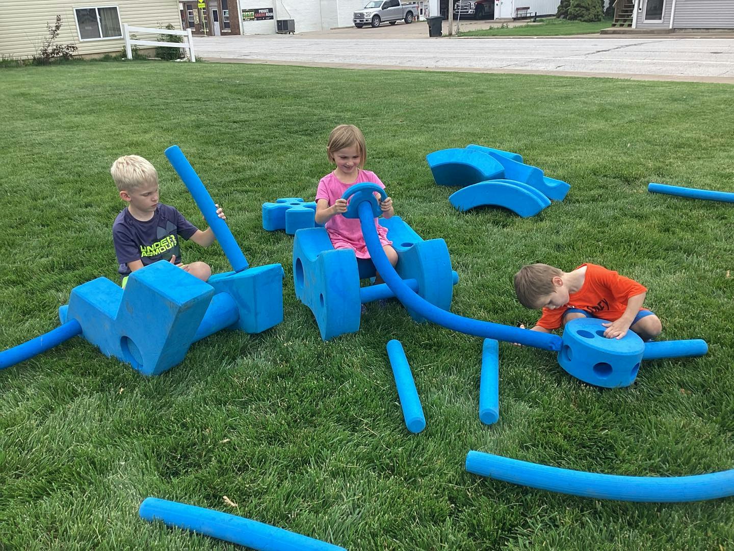 Children playing with large blue foam blocks on grass.