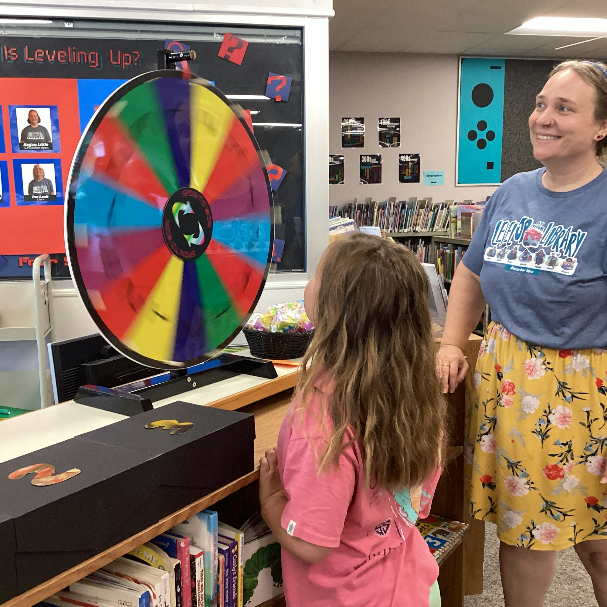 A colorful spinning wheel in a library setting with two people watching it.