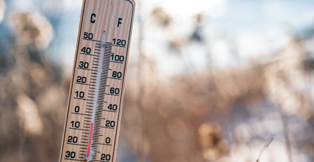 A close-up of a thermometer showing temperature in Fahrenheit and Celsius against a blurred winter background.