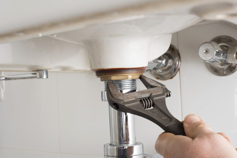A person is using a wrench to tighten or adjust a plumbing connection beneath a sink.