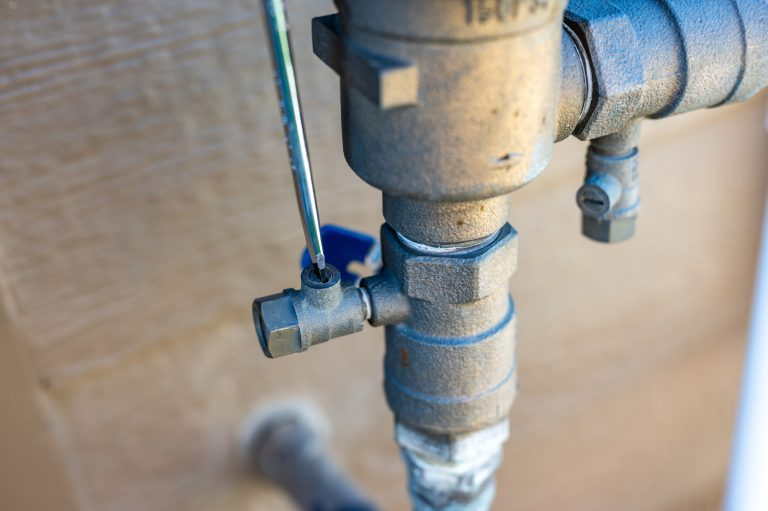 The image shows a close-up of a metallic valve with a wrench adjusting it, likely part of a plumbing or irrigation system.
