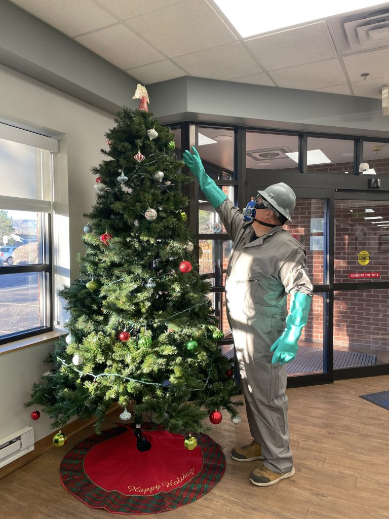 A person in protective gear decorates a Christmas tree indoors, spreading holiday cheer in a festive setting.