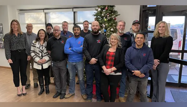 A group photo of a team with a Christmas tree in a cozy office setting, showcasing diverse individuals smiling together.