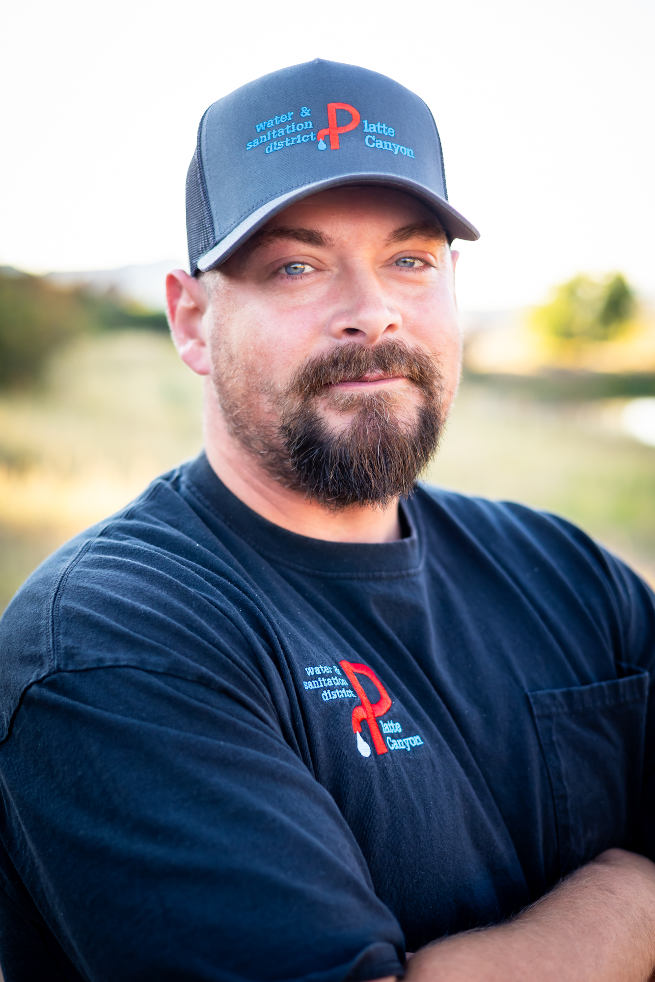 A man in a black shirt and baseball cap, standing outdoors against a blurred natural background.