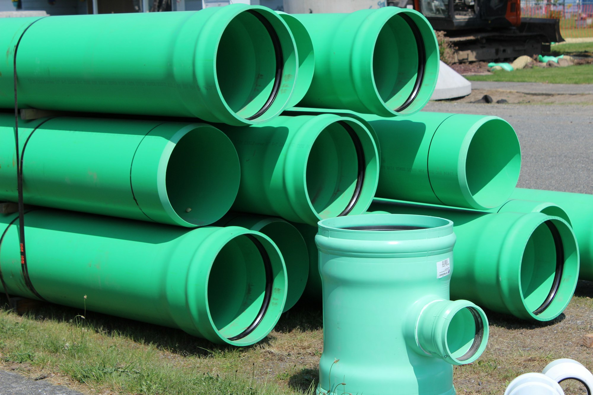 The image shows several green plastic pipes and fittings stacked on a grassy surface, likely for construction or plumbing use.