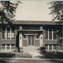 Grayville Carnegie library, a vintage photo of a classic brick building with stairs leading to the entrance and trees framing the scene.