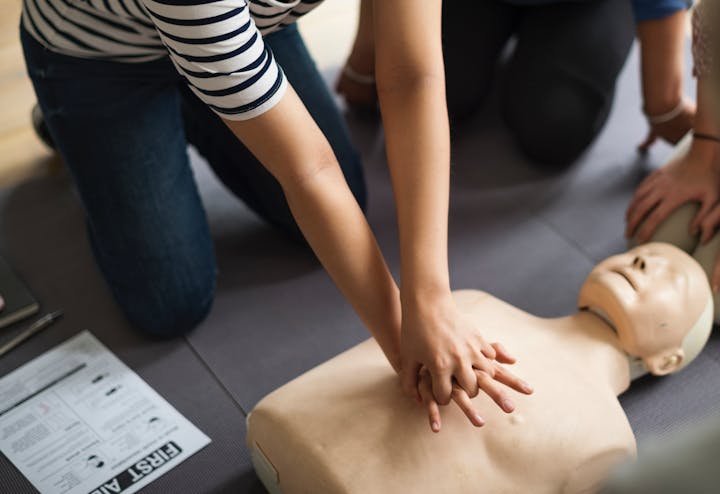 A person practicing CPR on a training mannequin, demonstrating first aid techniques with others nearby.
