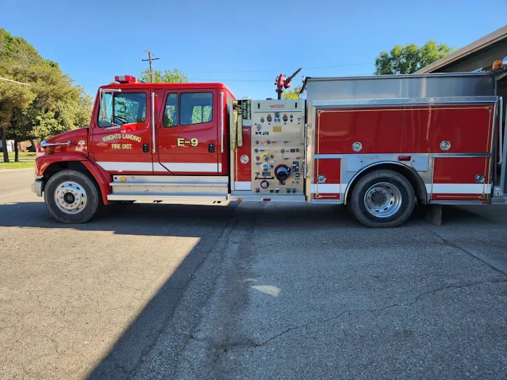 A red fire truck labeled "E-9" from Knights Landing Fire District parked on a street in sunny weather.