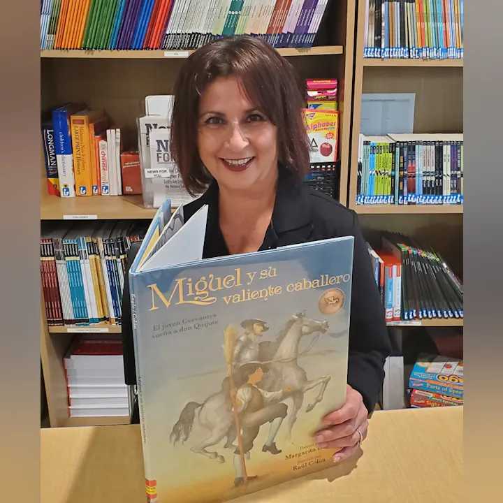 A person holding the book "Miguel y su valiente caballero" in a library.