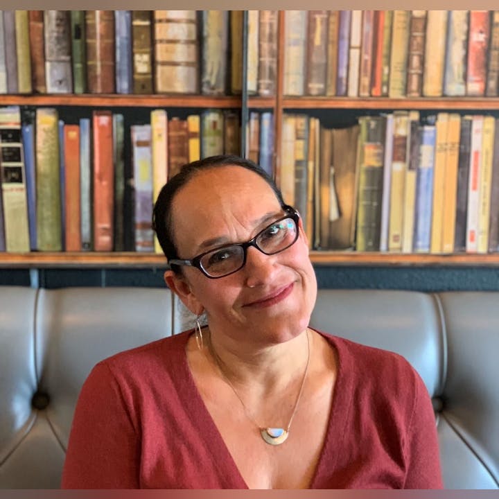 A person wearing glasses sits in front of a bookshelf, smiling.