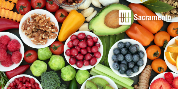 The image features a colorful array of fruits, vegetables, nuts, and herbs arranged on a surface, promoting healthy eating.