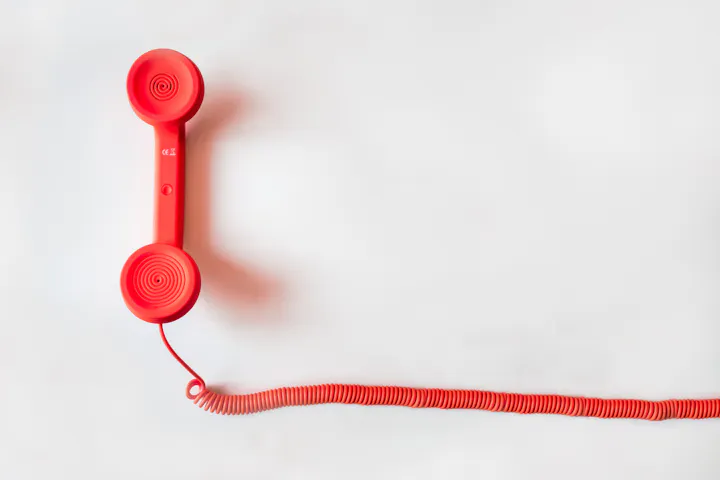A bright red vintage-style telephone handset with a coiled cord on a plain background.