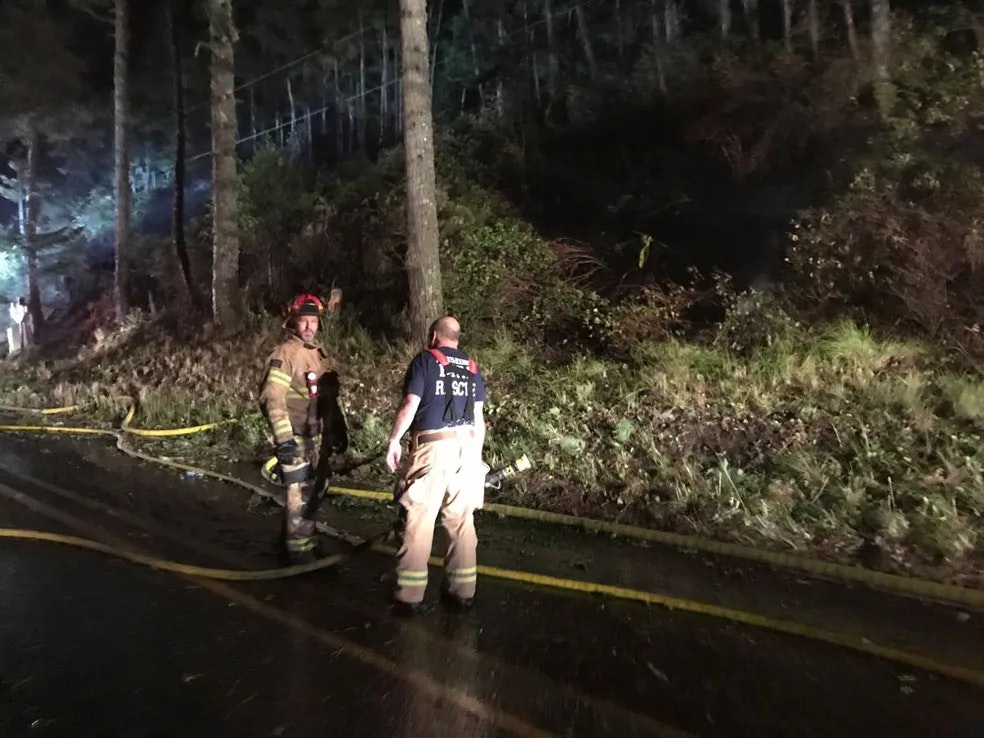 fire fighter illuminated at night talking to another fire fighter, fire hoses running on the ground between them