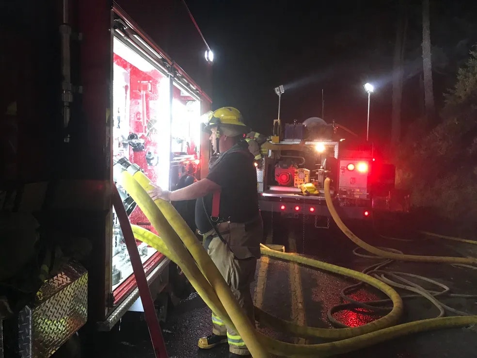 fire fighter at night standing in the light of a fire truck by the hoses
