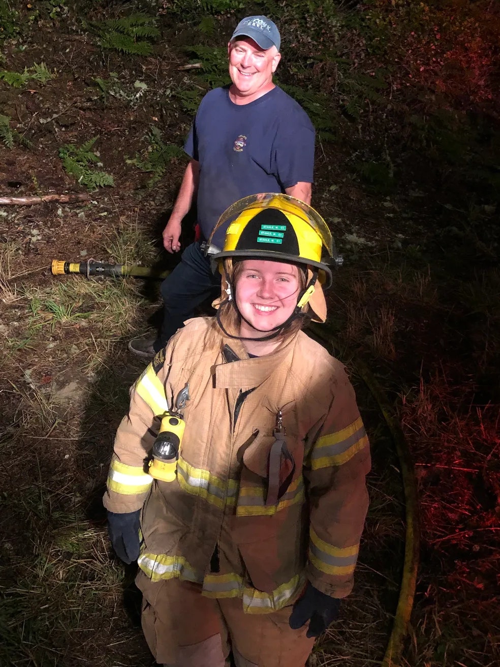 a fire fighter in full uniform standing in front of a fire fighter in plainclothes or a civilian