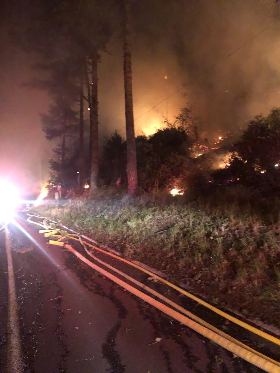 Distant shot of fire in a field at night, smoke rising.